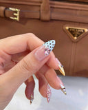 Luxury press-on nails featuring 3D pink flowers and star charms against a designer leather handbag background